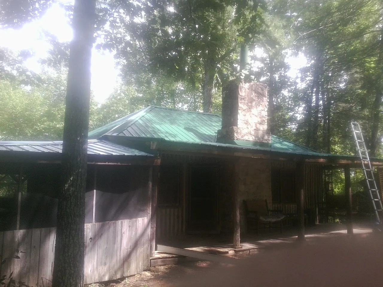 Green metal roof and stone chimney above a log cabin porch in Scottsville