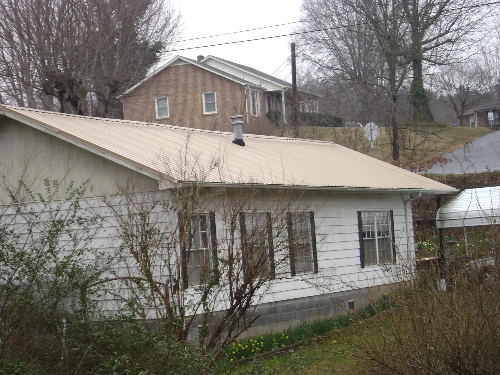 Tan metal roof on a white sided house set into a hillside — Commercial Roofing by Roofing Brothers in Scottsville